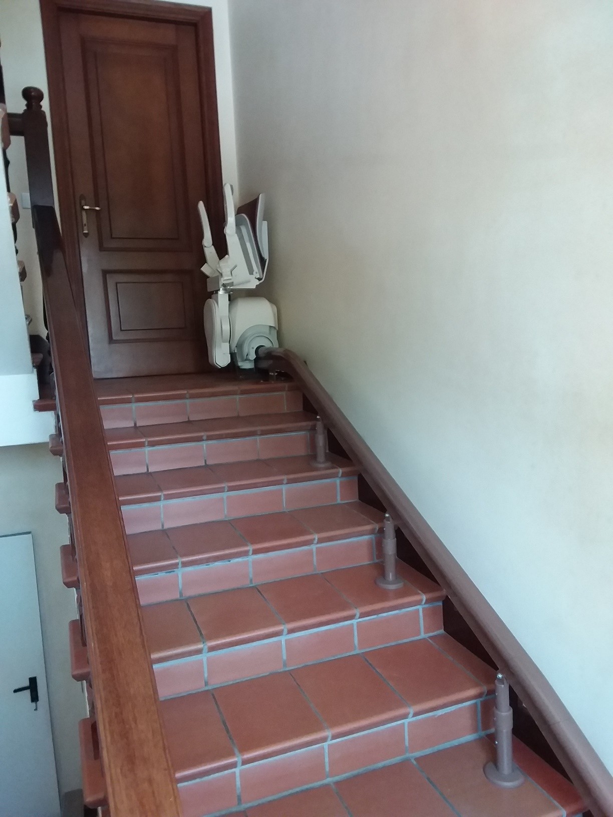 Montascale per interni su scala dritta in cotto, sedile pieghevole parcheggiato in stazione di arrivo con binario laterale.